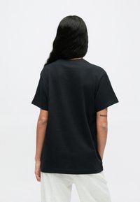 Juoda medvilninė marškinėliai laisvo silueto, trumpomis rankovėmis ir apvalia iškirpte. Galinė pusė išryškina jos lygią tekstūrą ir paprastumą.