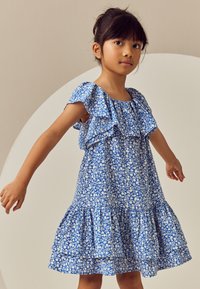 Robe bleue à motifs floraux blancs, manches à volants et jupe à étages. Tissu léger, encolure carrée et coupe décontractée.