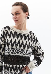 Sweter dzianinowy w kolorze kremowym z czarnymi geometrycznymi wzorami, z teksturowanym ciemnym paskiem, prążkowanym kołnierzem i mankietami, luźnym krojem oraz długimi rękawami.