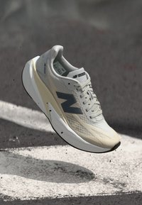 Basket légère en gris et beige, featuring une tige texturée, un logo 'N' proéminent et un design minimaliste avec une semelle rembourrée.