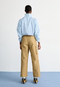 Šviesiai mėlyna trumpa striukė su gumine apdaila, derinama su smėlio spalvos cargo kelnėmis su šoninėmis kišenėmis ir sportiniais batais su geltonomis detalėmis.