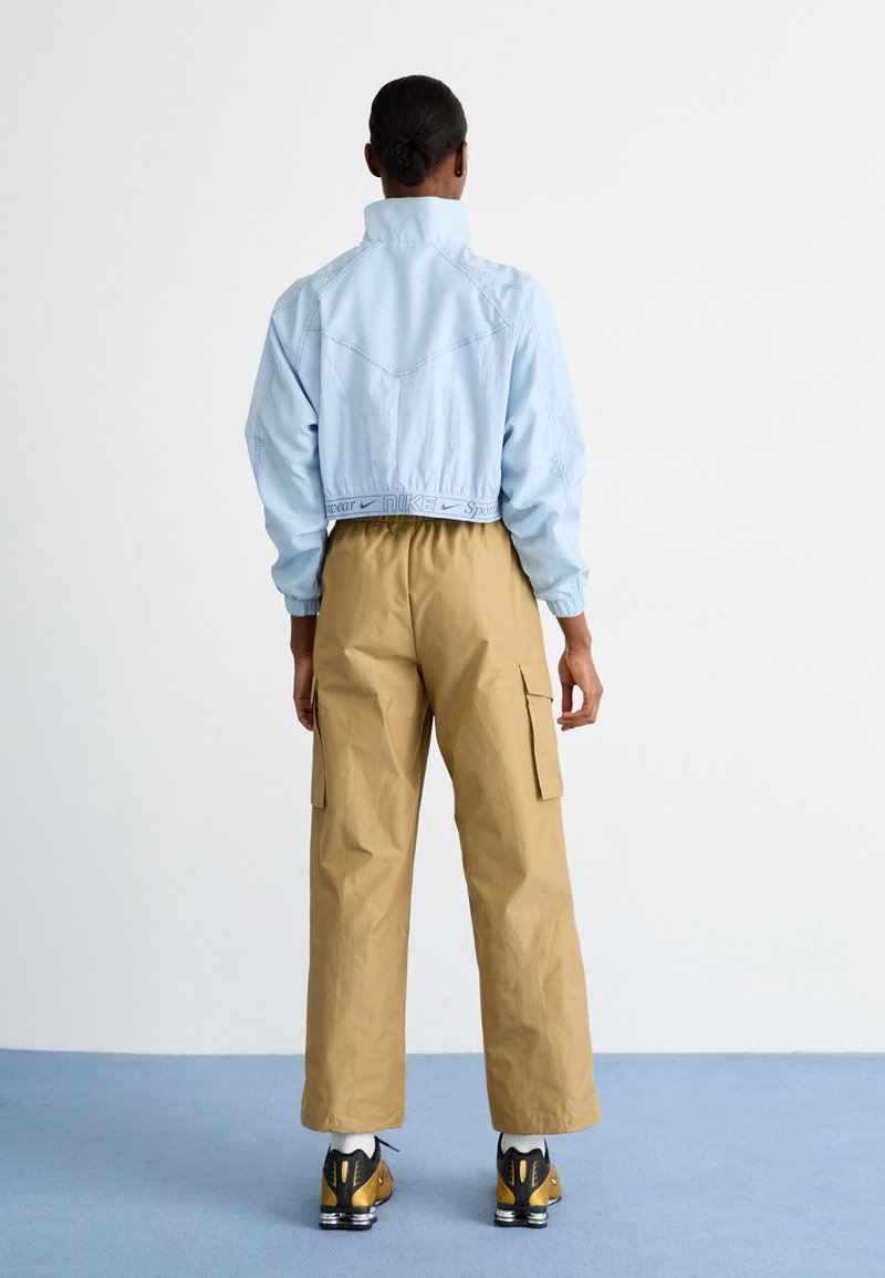 Giacca cropped azzurro chiaro con orlo elasticizzato, abbinata a pantaloni cargo beige con tasche laterali e sneakers con dettagli gialli.