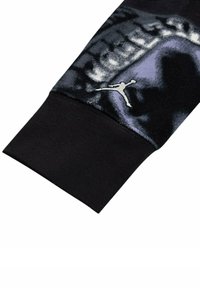 Manica di un maglione nero con un motivo testurizzato in diverse tonalità di grigio, con un logo Jumpman argentato sul polsino.