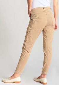 Pantalones cargo beige con un corte slim, que cuentan con múltiples bolsillos, una textura suave y una cintura de altura media. Llevados con mocasines de color claro.
