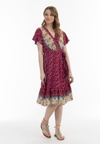 Rochie în fucsia, cu modele florale, mâneci scurte și evazate. Accentuata cu o bordură decorativă albastră și portocalie.