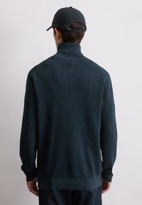 Ciemnozielony dziergany sweter z wysokim kołnierzem, ściągaczami na rękawach i dolnym brzegu. Tył ma bezszwowy wzór z teksturowanym wykończeniem.