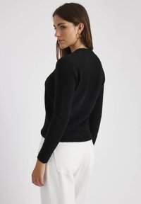 Pull noir ajusté en matière douce, avec des manches longues et un col rond, associé à un pantalon blanc. Design minimaliste.