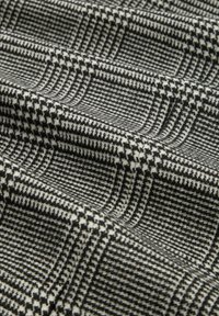 Tkana tkanina w czarno-białe wzory w pepitkę z teksturowanymi liniami, tworząca warstwowy i trójwymiarowy wygląd.