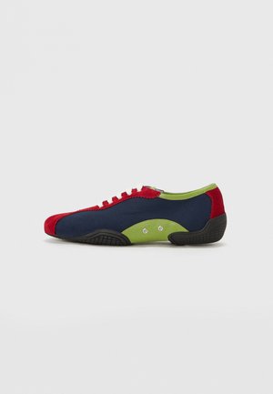 Zapatillas con parte superior azul marino, acentos de ante rojo en la puntera y el talón, panel lateral verde lima, cordones blancos y suela de goma negra con textura antideslizante.