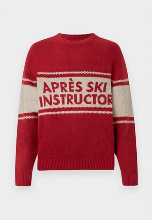 Pull rouge à col rond, avec une bande beige affichant "APRÈS SKI INSTRUCTOR," et un motif de tricot texturé. Manches et ourlet côtelés.
