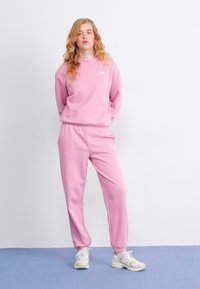 Ensemble sweat-shirt et pantalon rose, fabriqué en tissu doux. Doté d'un col rond, d'une taille élastique et d'un petit logo sur la poitrine.