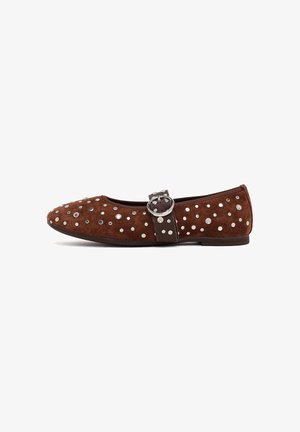 Bruine suède platte schoen met zilveren studs, een donkere band over de bovenkant en een ronde zilveren gesp op een witte achtergrond.