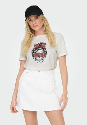 White t-shirt featuring a graphic of a skull wearing red polka-dot sunglasses and a matching bow, paired with a white denim skirt. Black cap worn.