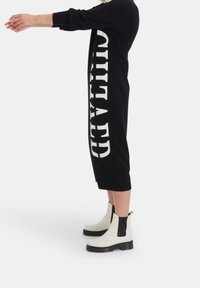 Svart stickad klänning med djärv vit text på sidan, mitt på vaden, med långa ärmar, kombinerad med vita ankelstövlar.