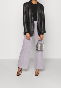 Svart läderblazer, åtsittande svart topp, vida lilafärgade texturerade byxor och en liten silverhandväska i ormskinn med kedjestropp. Svarta remsandaler.