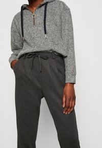 Grå zip-up hoodie med svarta dragsnören och en nyckelring på dragkedjan, kombinerad med mörkgrå sweatpants som har en dragsnörs-midja.