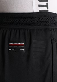 Shorts de sport noirs avec ceinture respirante, logo Nike FC, et patch texte indiquant « Sem Risco Não Há Vitória » et « 1994 » sur le côté gauche.