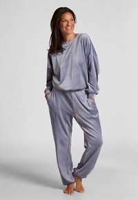 Lichtgrijs velours loungewear set bestaande uit een relaxed langermige top en taps toelopende broek, beide voorzien van zijzakken voor gemak.