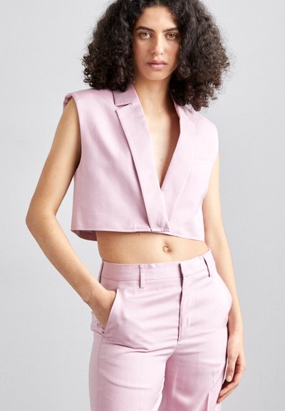 Světle růžový krátký blejzr bez rukávů, s hlubokým výstřihem do V a jednou kapsou. Slučuje se s odpovídajícími slim-fit kalhotami, vše vyrobeno z hladké látky.
