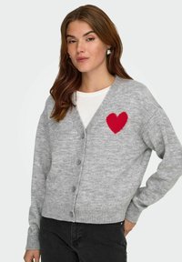 Cardigan grigio lavorato a maglia con scollo a V, caratterizzato da un ricamo di un cuore rosso sul lato sinistro del petto e chiusura con bottoni nella parte anteriore.