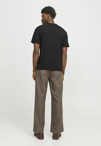 Sort bomulds T-shirt med korte ærmer, rund halsudskæring og afslappet pasform, parret med løse, beige bukser og brune fodtøj.