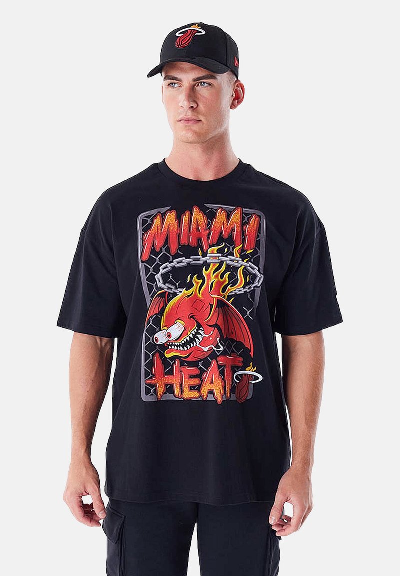 T-shirt nera oversize con grafica di una fiamma rossa e gialla rappresentante un pesce, accompagnata dalla scritta "MIAMI HEAT". Abbinata a un cappellino nero con logo.