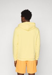Gul hættebluse med snørelukning og ribbede manchetter, parret med orange shorts. Stoffet ser blødt og afslappet ud.