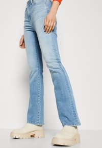 Ljusblå utsvängda jeans har en klassisk denimtextur, en figursydd midja och en något sliten finish, tillsammans med klumpiga krämfärgade plattformsskor.