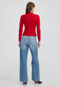 Czerwona bluzka z długim rękawem i wysokim kołnierzem, zestawiona z jasnoniebieskimi spodniami dzwonami. Spodnie posiadają tylne kieszenie i wyblakły odcień.