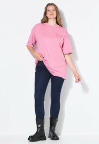 Camiseta de algodón rosa con mangas cortas y escote redondo, con bordado en el pecho. Combinada con jeans ajustados de color azul oscuro y botas negras.