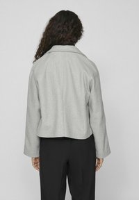 Šedá zkrácená bunda s límcem a širokými rukávy, vyrobená z texturované tkaniny. Záda mají jednoduchý design s viditelnými švy.