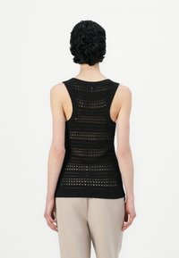 Svart strikket tanktop med teksturert mønster som har åpen arbeid detaljer. Ermeløs design, ribbestrikket hals og nederkant.