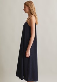 Navyblaues Sundress mit dünnen Trägern, das ein fließendes Design und texturierten Stoff aufweist. Fällt unter die Knie und hat eine gerade Silhouette.