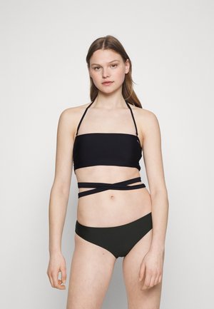 Schwarzer Bandeau-Bikini-Oberteil mit Halterneck-Trägern und überkreuzten Details, kombiniert mit dunkelgrünen Bikini-Unterteilen. Glattes, dehnbares Material.