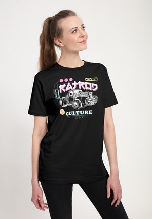 Junge Frau in schwarzem Grafik-T-Shirt mit einem Vintage-Lkw und dem Schriftzug „Patrol Culture“, die mit einem leichten Lächeln nach oben blickt.