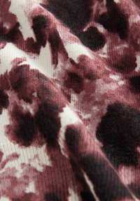 Gros plan sur un tissu doux avec un motif abstrait animalier en bordeaux, noir et blanc, et une texture tricotée visible.