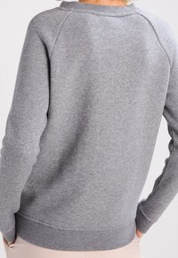 Šedá mikina s žebrovaným lemem a manžetami, raglánovými rukávy a měkkou texturou. Disponuje minimalistickým designem bez výrazných vzorů.