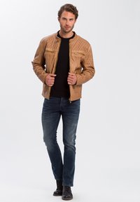 Skórzana kurtka zapinana na zamek w kolorze brązowym, z pikowanym wzorem na ramionach, dwiema kieszeniami na zamek, w połączeniu z niebieskimi dżinsami i czarnymi sznurowanymi botkami.