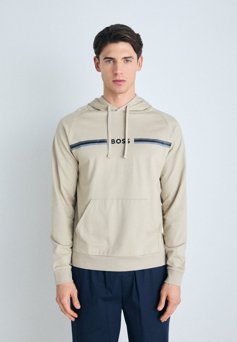 Felpa beige con tasca a marsupio, caratterizzata da una striscia orizzontale blu navy e logo "BOSS" sulla parte anteriore. Tessuto morbido e liscio.