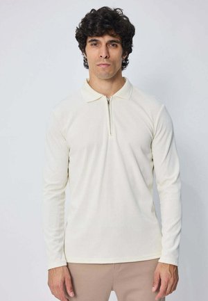 Polo à manches longues en tissu côtelé blanc cassé avec un col zippé quart et un col pointu, doté d'une silhouette ajustée.