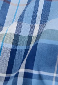 Gros plan sur un tissu à carreaux bleu, blanc et beige avec des rayures verticales et horizontales qui s'entrecroisent et une texture tissée visible.