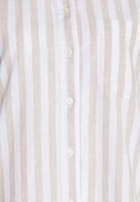 Linen shirt featuring alternating beige and white vertical stripes, with a button front and a chest pocket. Soft texture and classic design.