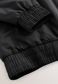 Manche et ceinture de veste noire avec poignets côtelés élastiques et texture de tissu lisse.