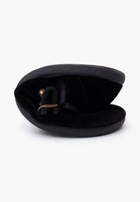 Runder schwarzer Koffer aus strukturiertem Kunstleder mit einem weichen Samtinnenraum, ausgestattet mit einem bronzefarbenen Verschluss und einem schlanken, kompakten Design.