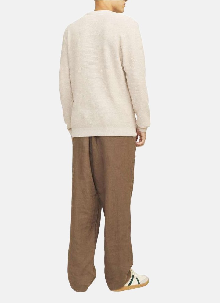 Un pull texturé beige clair avec une coupe décontractée, associé à un pantalon en lin brun ample et des chaussures blanches avec des accents verts.