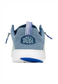 Zapato slip-on de denim azul con suela blanca, que presenta un upper de tela texturizada, parche de logo azul y tiradores azules en contraste.