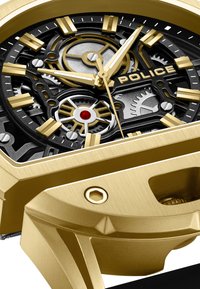 Złoty zegarek z czarną tarczą skeleton, srebrnymi akcentami oraz czerwonym detalem. Posiada teksturowaną złotą obudowę i wyraźne znaczniki godzin.