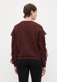 Sweatshirt bordeaux com detalhes em tule franzido nas mangas, tecido suave, corte descontraído e gola redonda. Combinado com calças pretas.
