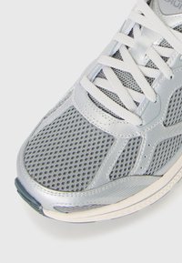 Gray and white breathable mesh athletic shoe with white laces and silver synthetic overlays on a white background.