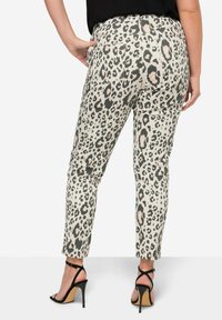 Pantalons chevilles à imprimé léopard en beige et noir, avec poches arrière et coupe slim. Portés avec des talons noirs à lanières, mettant en valeur un design ajusté.